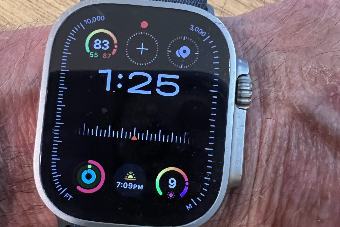 Close view of the Apple Watch Ultra 2 face showing large blue numerals reading 1:25, a heart rate of 83 beats per minute, activity rings, and a sunset time of 7:09 PM.